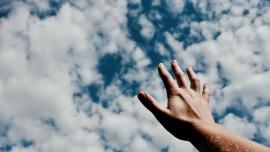 يد ممتدّة إلى سماء مليئة بغيوم بيضاء. 